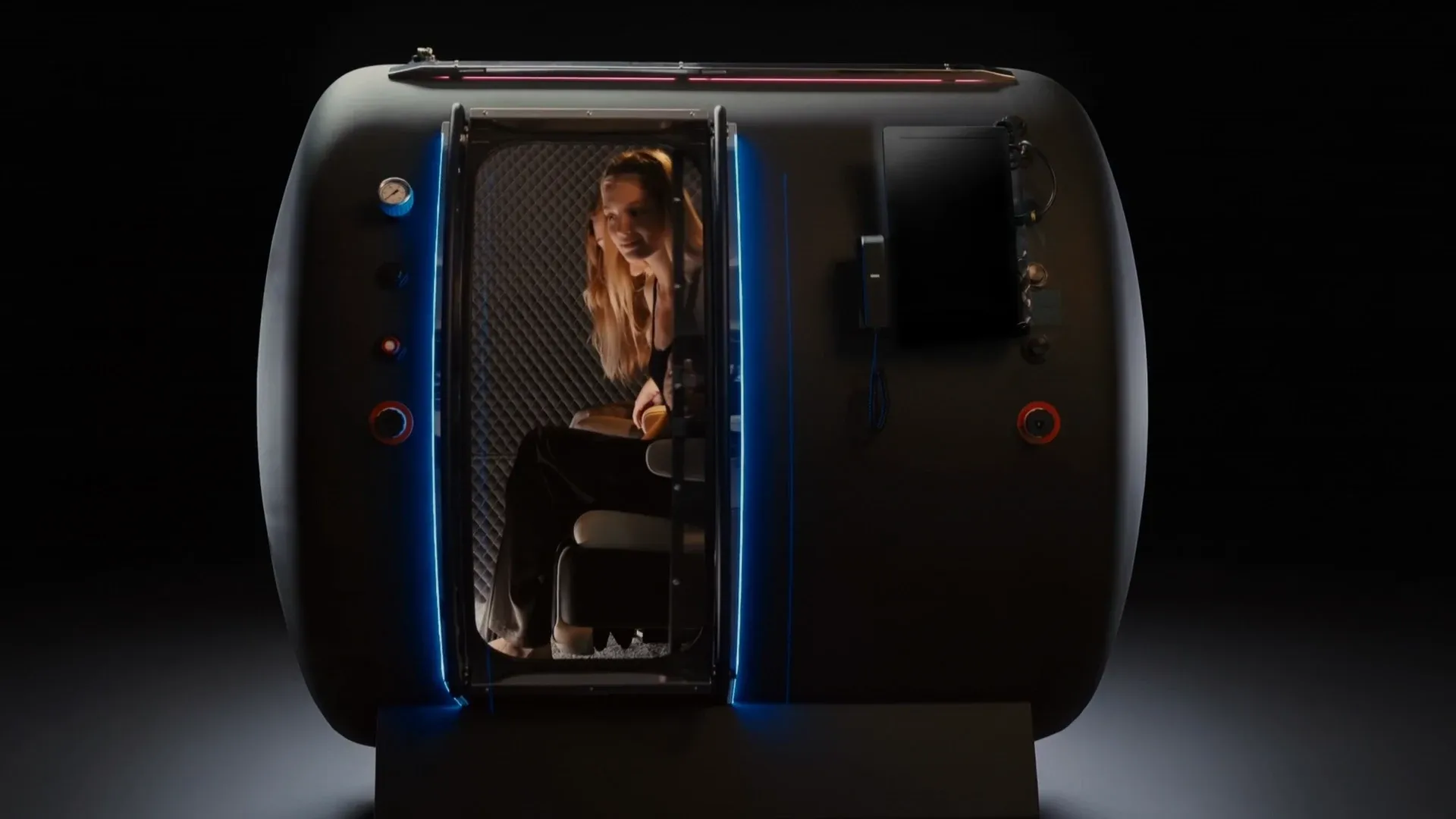 A Superhuman chamber on a dark set with its door open, a guest seated inside