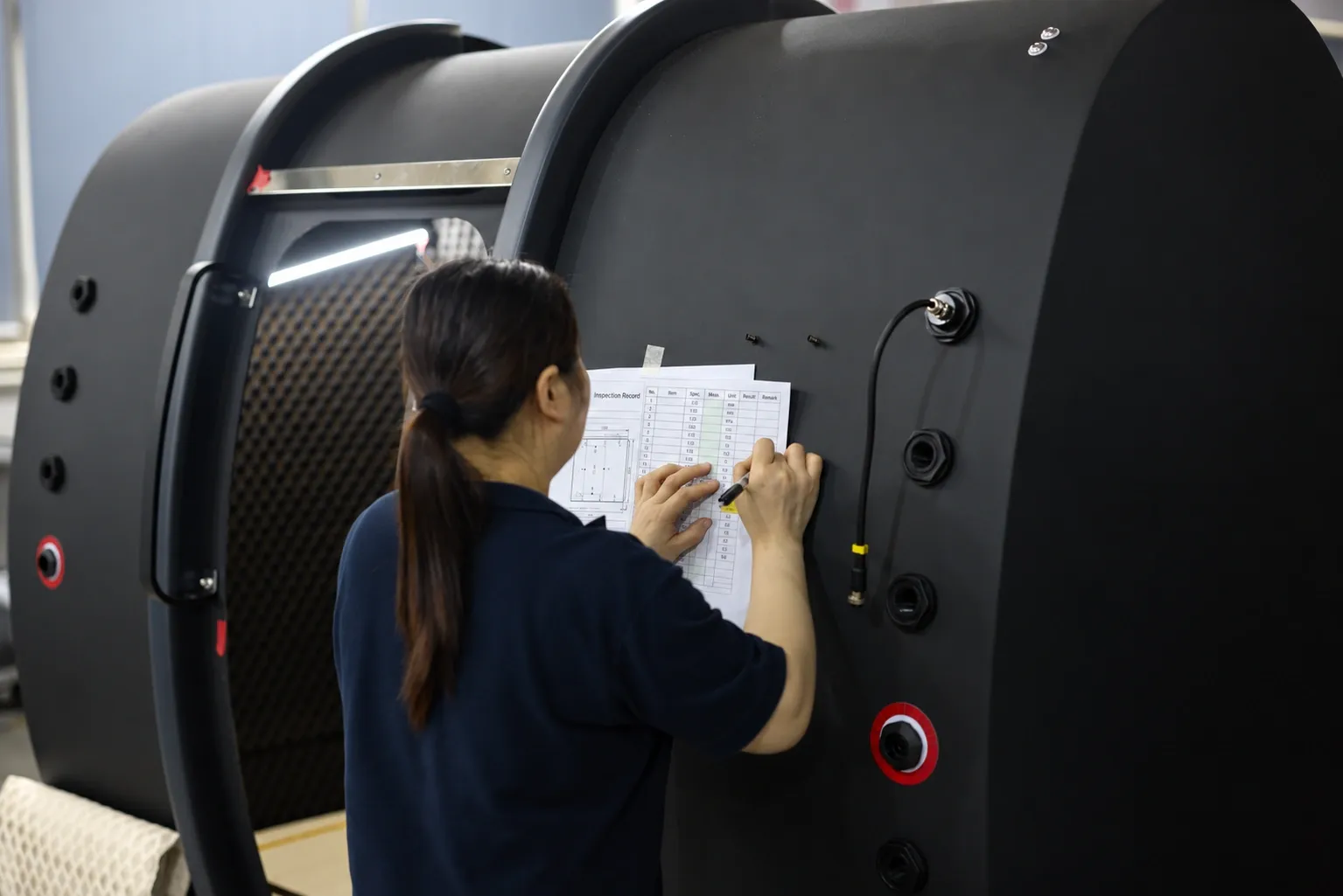 A quality-control inspector recording measurements against the build checklist taped to a Superhuman chamber