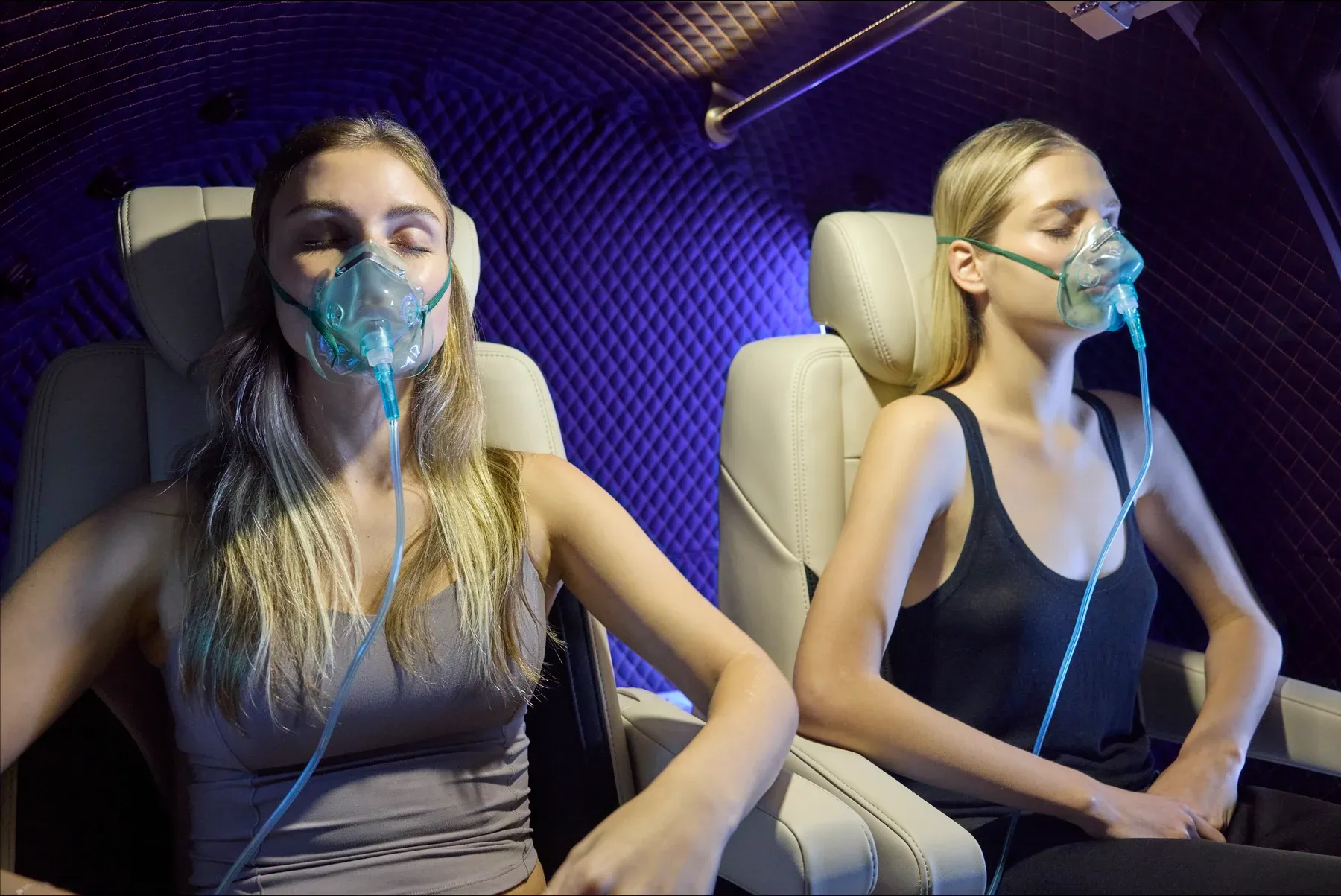 Two guests reclined in cream leather seats inside the T2, eyes closed, wearing oxygen masks